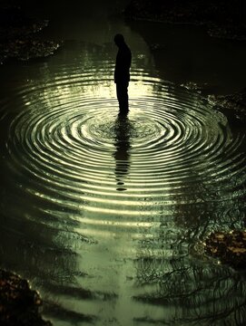 A silhouette of a person jumping off a cliff into a crystal-clear lake, the splash sending ripples across the water. 