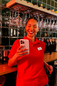 Smiling waitress using smartphone in front of bar counter