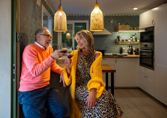 Cheerful mature diverse couple enjoying wine and laughter at home