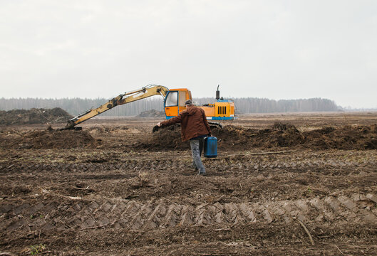 A man carries a fuel canister to an excavator.