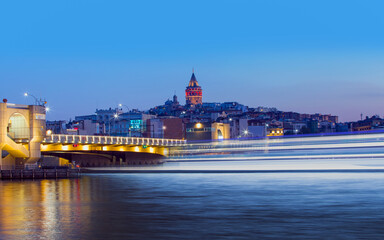 Obraz premium Galata Tower, Galata Bridge, Karakoy district and Golden Horn with motion speed light of passing ferry in the foreground at night istanbul - Turkey 