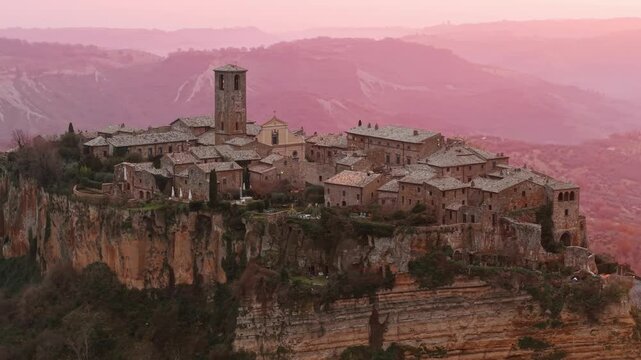 Aerial view of Civita di Bagnoregio, a picturesque village located on a plateau in central Italy, illuminated by a beautiful pink sunset light
