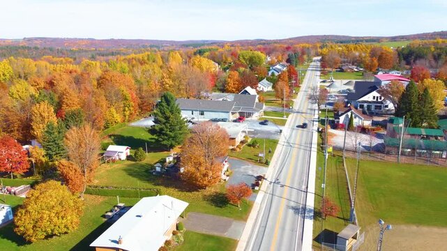 Two cars driving on the national highway and passing through a small town in Estrie with the trees colored with the Autumn colors