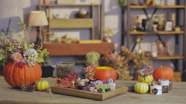 A cozy autumn-themed table arrangement featuring floral pumpkin centerpieces, succulents, candles, and rustic decor in a warmly lit indoor setting.