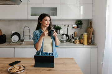 Young Woman Drinking Coffee While Working on a Tablet in a Kitchen