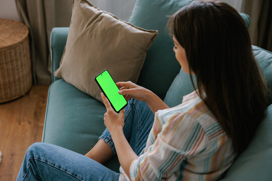 Woman Relaxing on Couch Using Smartphone with Green Screen Display