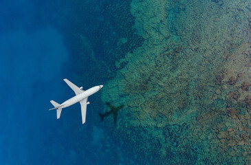 Airplane flying over clear blue ocean with reef visible below