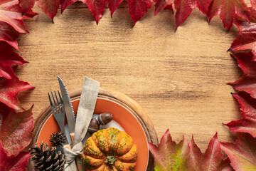 Thanksgiving frame made of autumn leaves with copy space and plate with cutlery and pumpkins