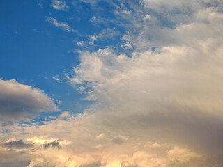 Sky filled with soft, white clouds scattered across a vibrant blue expanse. Sunlight gently illuminates the cloud formations creating a peaceful, airy scene.