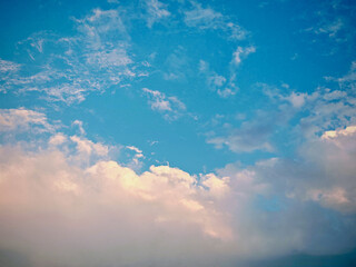 A vibrant blue sky is partially covered with soft, fluffy white clouds. The lower edges of some...
