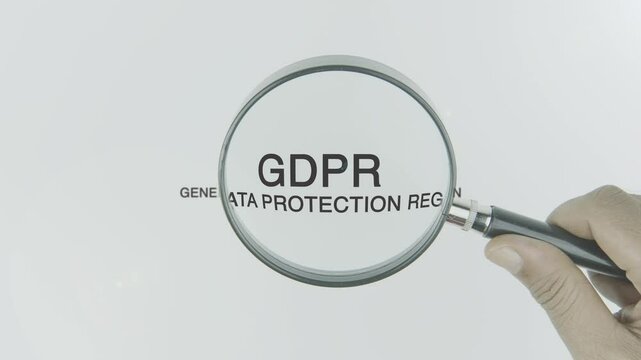 GDPR (General Data Protection Regulation) text or word highlighted by a magnifying glass in a hand on a white background, symbolizing data privacy, protection, and compliance in the digital age
