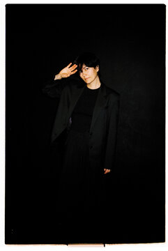 Female dressed in black poses with a salute against a dark background
