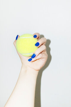 Hand with blue nails manicure holding neon green sport tennis balls