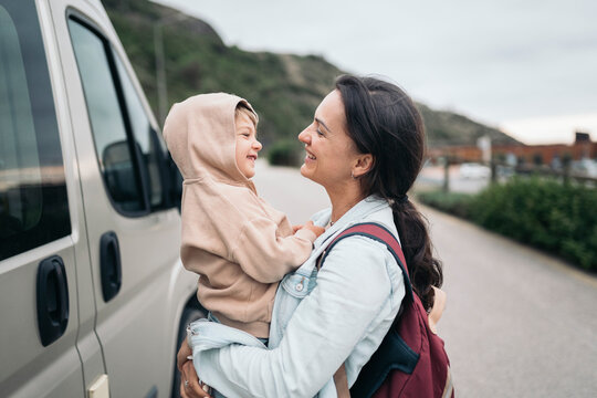 Mother holding smiling son next to minivan on road trip