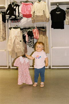 Little baby girl choosing the dress in the shop.