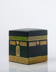 A miniature replica of the Kaaba, Islam's holiest site, sits on a white background. The intricate gold detailing on the dark green box stands out.
