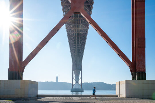 Fototapeta Jogger running beneath a large suspension bridge in sunlight