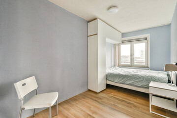 A clean and stylish bedroom featuring a bed, a chair, and natural light flowing through the window, emphasizing simplicity and comfort in design.