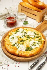 Italian pizza with cheese and pesto sauce on a wooden board.
