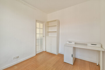 Bright and simplistic room featuring a white desk, shelving unit, and an inviting wooden floor that promotes a calm atmosphere for work or relaxation.