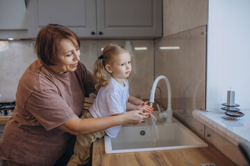 Grandma teaches her granddaughter to wash her hands and helps her in the kitchen