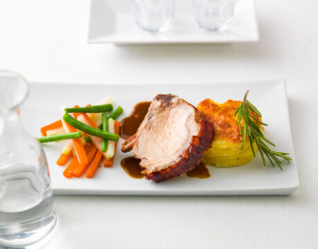 gourmet dish featuring a slice of roast pork with potato gratin