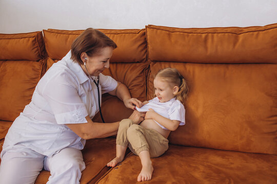 Doctor woman doing examination to little girl child baby sitting on sofa, home care