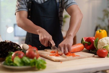 Chef chopping carrots on cutting board, surrounded by fresh vegetables