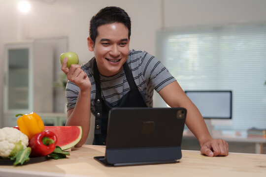 Smiling chef holding green apple having video call on tablet in kitchen