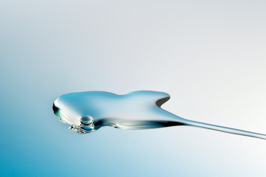Droplet of fluid face serum on light blue gradient backdrop.