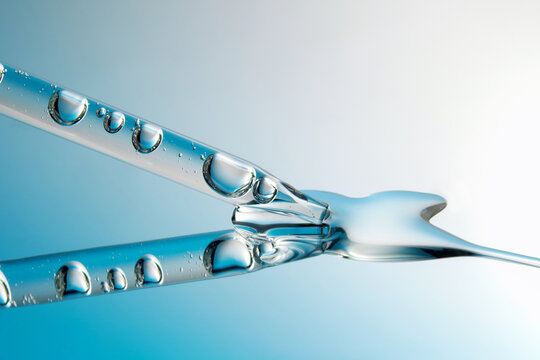 Close up of a pipette with liquid on reflective blue background.