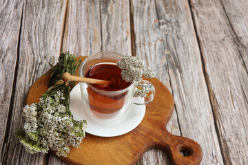 A cup of yarrow tea with fresh yarrow flowers on wooden table