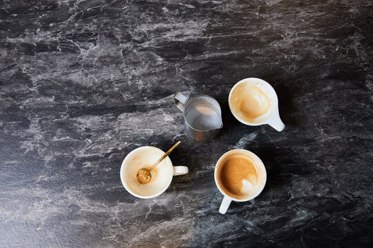 Empty Coffee Cups and Milk Frothing Pitcher on Dark Marble Surface