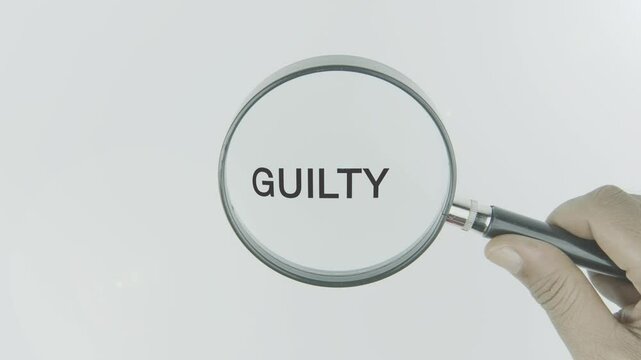 Guilty text or word highlighted by a magnifying glass in a hand on a white background, symbolizing feelings of responsibility, remorse, and accountability