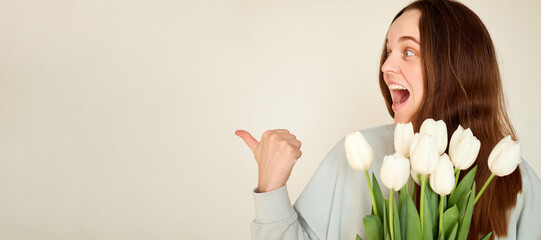 A woman with long brown hair smiles enthusiastically while holding a bouquet of white tulips. She...