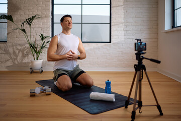 Fitness instructor doing breathing exercise while live streaming his exercise class at home.