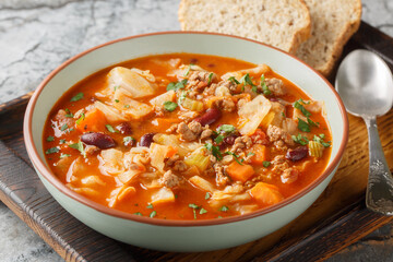 Yummy beef and cabbage soup with additional ingredients are tomato, kidney beans, carrot and celery closeup in the plate on the table. Horizontal
