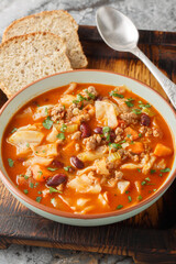 Ground beef cabbage soup, with red bean, onion, tomatoes, carrots and celery closeup in the plate on the table. Vertical