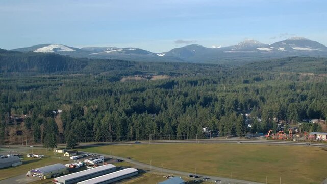 Buildings and Cars on the Road next Forest Landscape with Distant Mountains Aerial View
