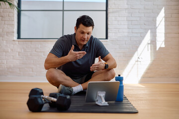 Personal trainer making video call over touchpad from his fitness studio.