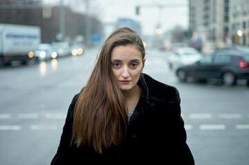 Woman with long hair wearing a black coat stands in a busy city street. Berlin, Germany