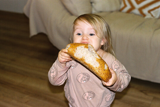 Little cute baby girl eating fresh bread at home.