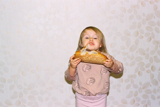 Little cute baby girl eating fresh bread at home.