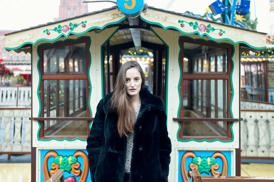 Woman in a fur coat standing in front of a decorative vintage ferris wheel with festive decor. Berlin, Germany