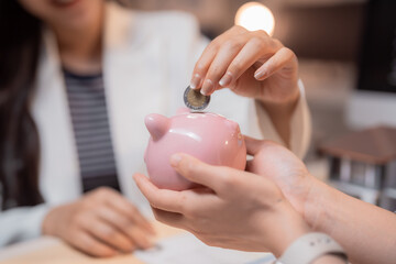 Businesswoman and client are inserting coin into piggy bank, saving money for future investment in real estate market, financial planning and savings concept