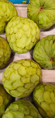 Green cherimoya fruits with scaly skin are placed in a carton tray; some have a smooth surface, while others have slight blemishes and brown spots;