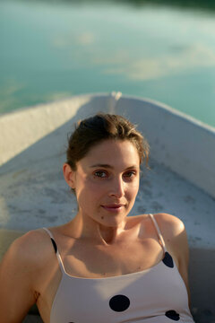 Woman in a polka dot dress relaxing in a boat under sunlight, beside a calm lake. Brandenburg, Germany
