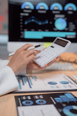 Businesswoman wearing white suit sitting at desk and analyzing financial charts displayed on...