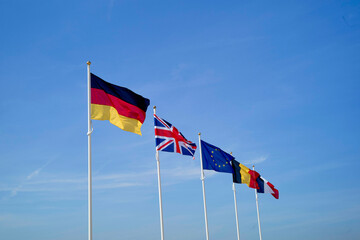 Five flags representing Germany, UK, EU, France, and Belgium waving against a clear blue sky. Hauts-de-France, France