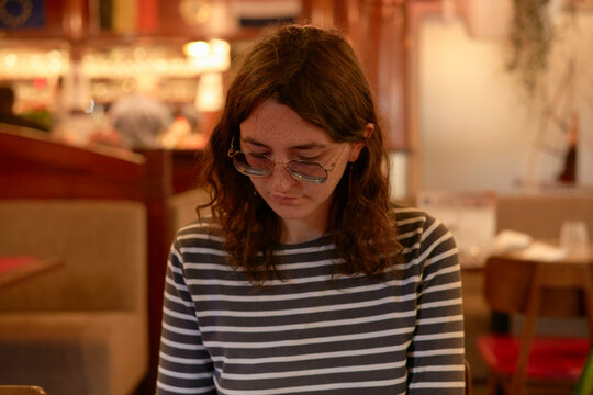 Woman with glasses and striped shirt sitting in a cozy cafe interior studying the menu. Hauts-de-France, France